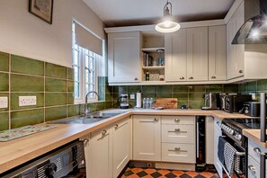 A kitchen with white cabinets, a green tiled backsplash, a wooden countertop, and a black stove. - Host & Stay | Lavender Cottage SLEA (Pointon)