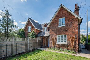 A two-story brick house with a front porch, a fenced yard, and a clear sky. - Host & Stay | Lavender Cottage SLEA (Pointon)