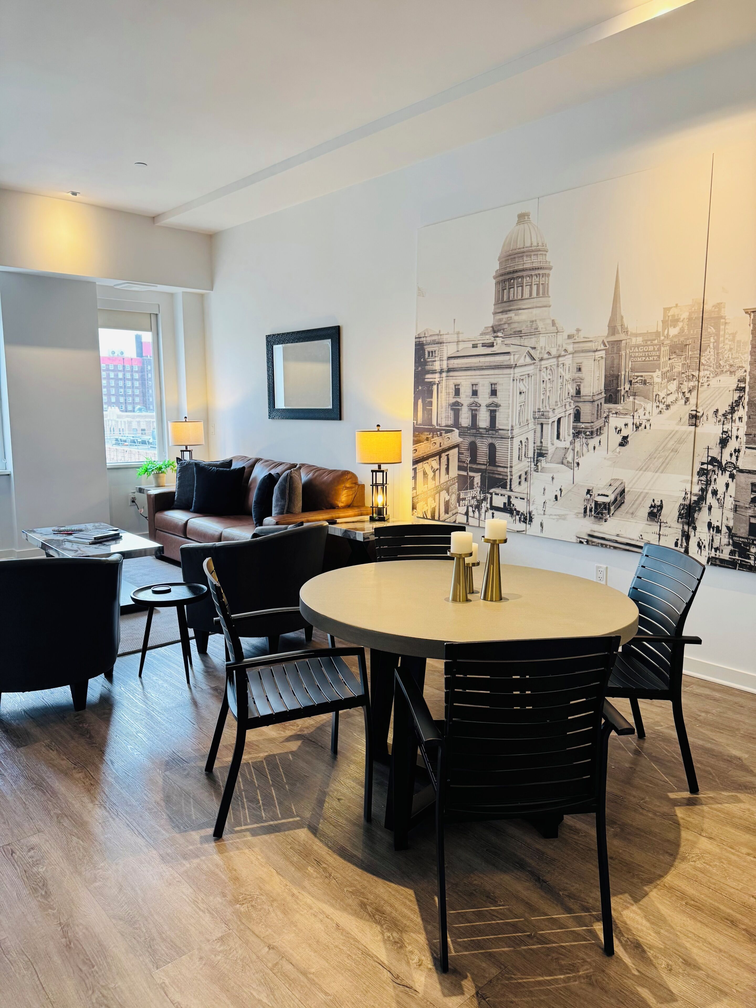 Ein modernes Wohnzimmer mit einem runden Esstisch, schwarzen Stühlen, einer Couch und einer großen Wandmalerei mit Stadtansicht.