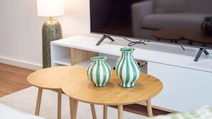 Un saló modern amb un televisor de pantalla plana, una taula còmoda blanca i dos vasetes amb ratlles sobre una taula de fusta.