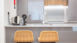 A modern kitchen with a Bosch refrigerator, a coffee maker, and a kettle on the counter. There are two wicker chairs in front of the counter. - Polacos Residence | 1BR | Apt M by LovelyStay (Vila Nova de Gaia)
