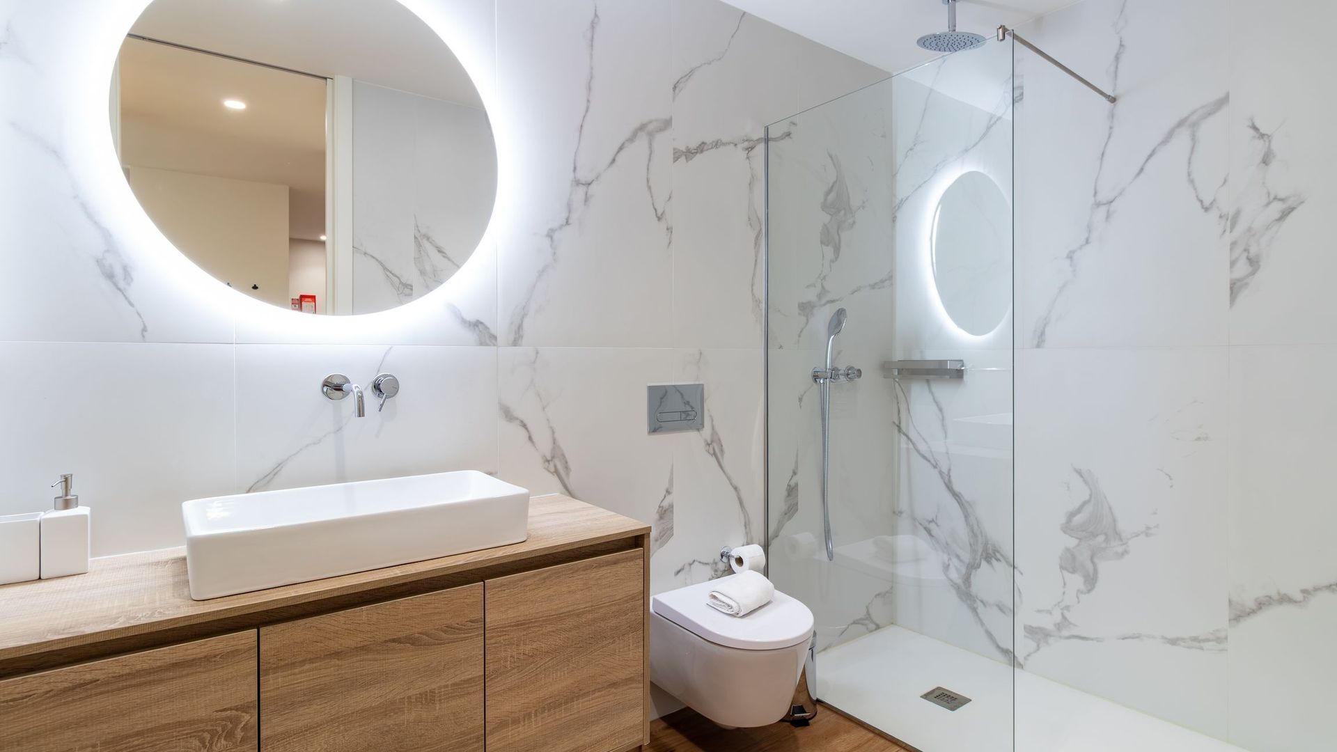 A modern bathroom with a rectangular sink, wooden vanity, a toilet, and a glass-enclosed shower area.