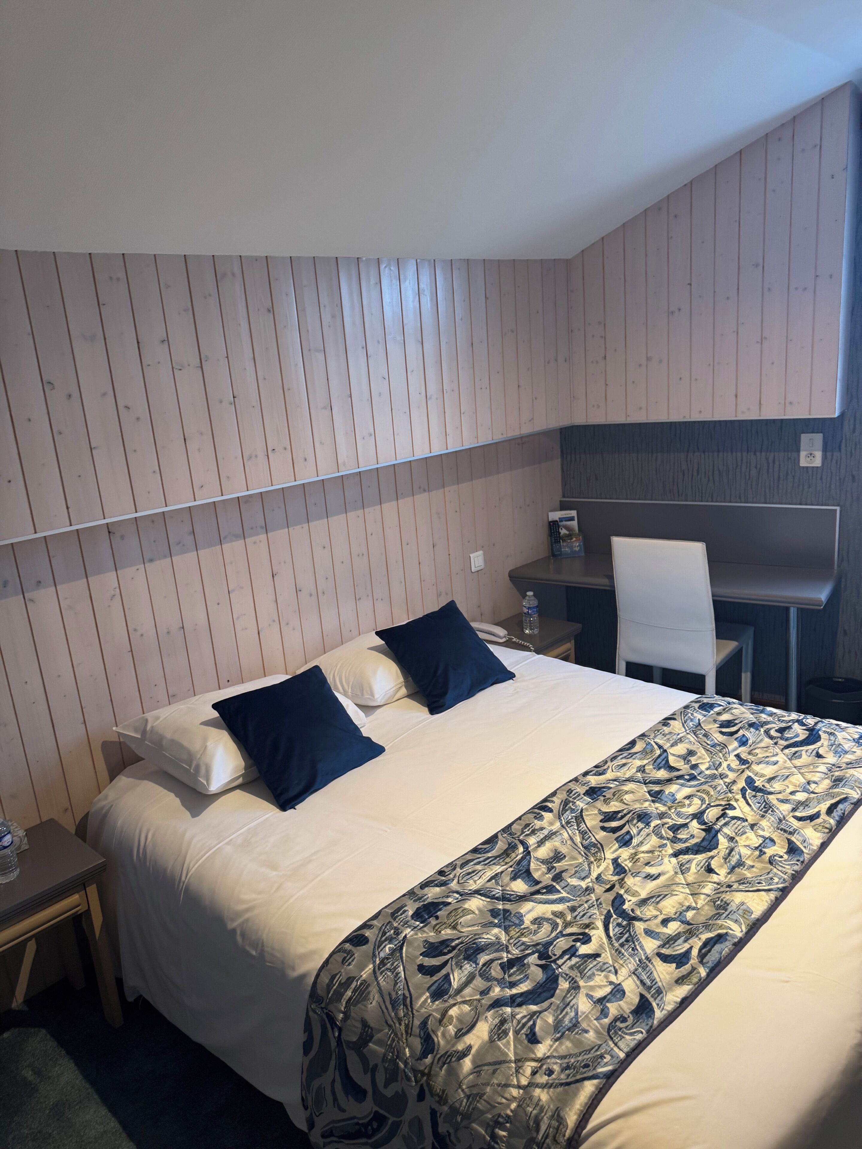 A hotel room with a bed, a desk, a chair, and a small table.