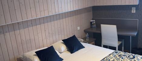 A hotel room with a bed, a desk, a chair, and a small table.