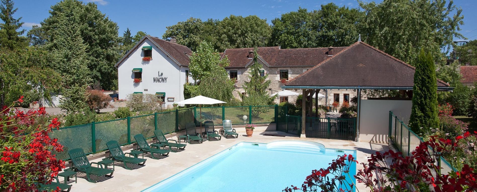 A pool area with lounge chairs, a building labeled 'Le MACNY,' and a fenced garden.