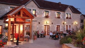 A stone building with a covered outdoor seating area and multiple windows with flower boxes. - restaurant hôtel le magny (Les Riceys)