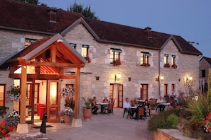 Een stenen gebouw met een overdekte zitplaats buiten en meerdere ramen met bloembakken.