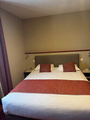 Een hotelkamer met een groot bed, twee kussens, een nachtkastje en een waterfles.