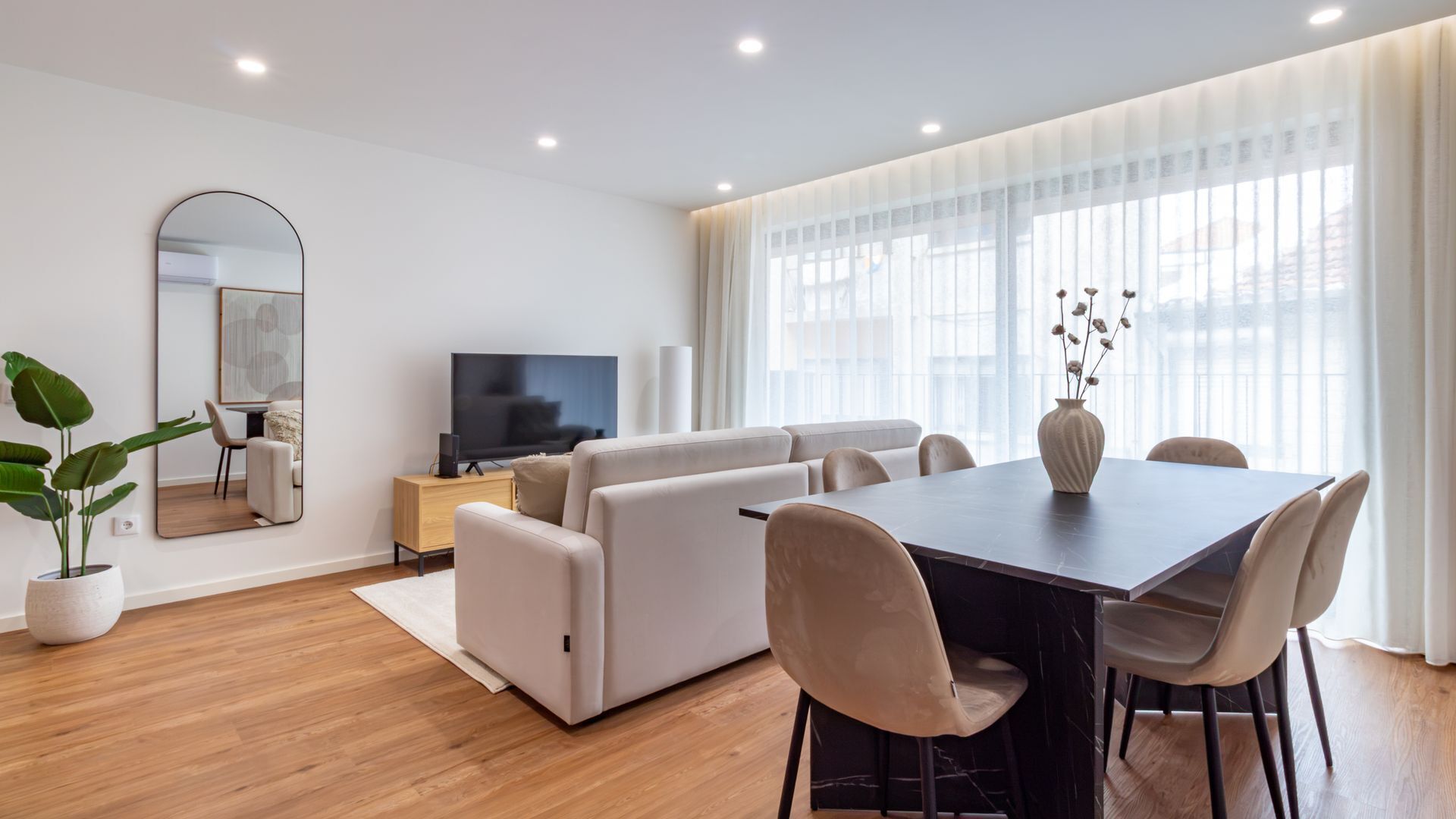 Un salon moderne comprenant un ensemble de canapés, une table à manger avec des chaises, un téléviseur à écran plat et une grande fenêtre ornée de rideaux légers.