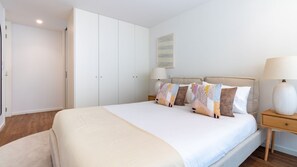 Un dormitorio con una cama grande, varios almohadones, una mesita de noche, una lámpara y un armario.
