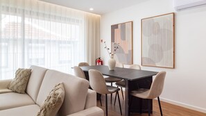 Ein modernes Wohnzimmer mit Sofa, Esstisch und Stühlen. An der Wand hängen zwei gerahmte Kunstwerke.