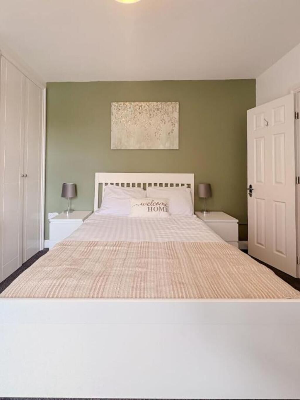 Ein Schlafzimmer mit einem Bett, zwei Nachttischen, einer Kommode, einer Tür und einem Wandbild.