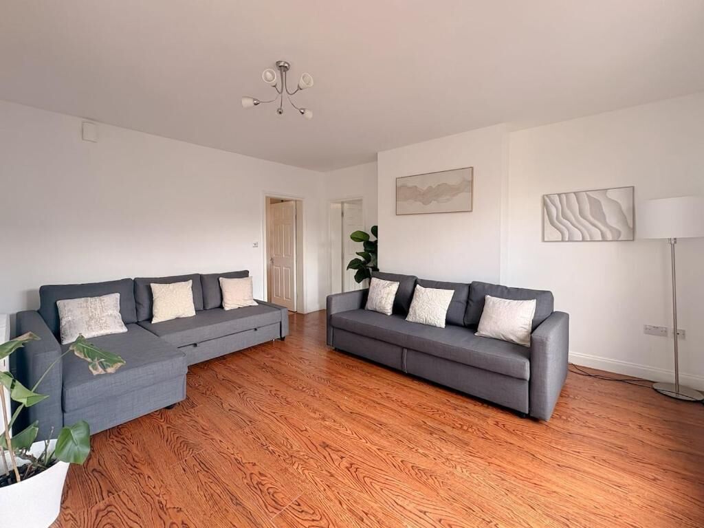 Ein geräumiges Wohnzimmer mit zwei grauen Sofas, einem Holzboden, einer Topfpflanze und einer Stehlampe.