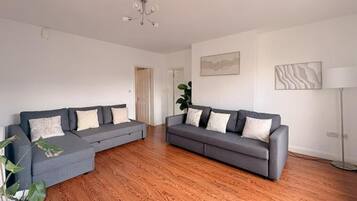 Ein geräumiges Wohnzimmer mit zwei grauen Sofas, einem Holzboden, einer Topfpflanze und einer Stehlampe.