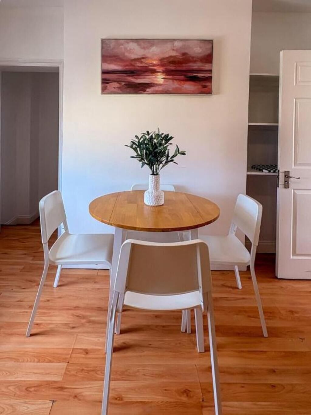 A dining area with a round wooden table, white chairs, and a potted plant.
