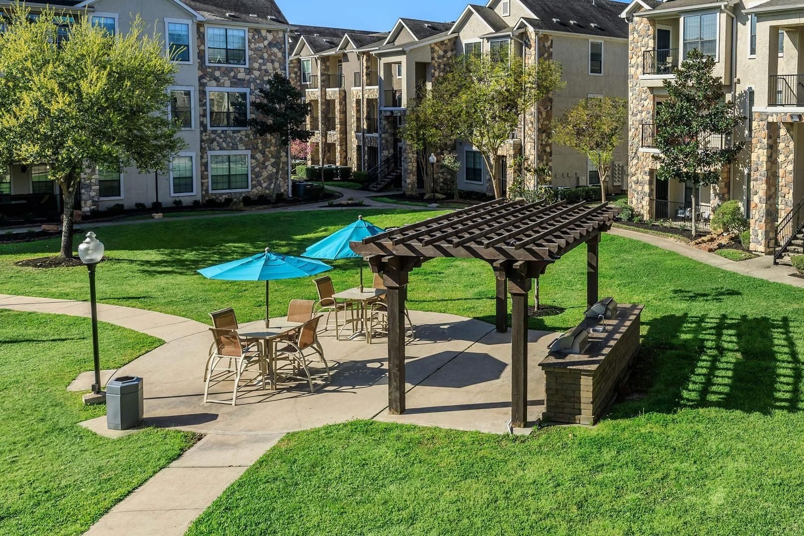 A courtyard with outdoor seating, a pergola, and stone buildings in the background.