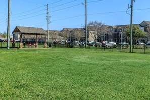 A grassy area with a gazebo, a fenced parking lot, and residential buildings in the background. - Landing Chic 1bd, Clubhouse, Gym (Katy)