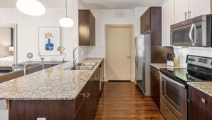 A modern kitchen with granite countertops, stainless steel appliances, and a wooden floor. - Landing Chic 1bd, Clubhouse, Gym (Katy)