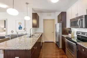A modern kitchen with granite countertops, stainless steel appliances, and a wooden floor. - Landing Chic 1bd, Clubhouse, Gym (Katy)