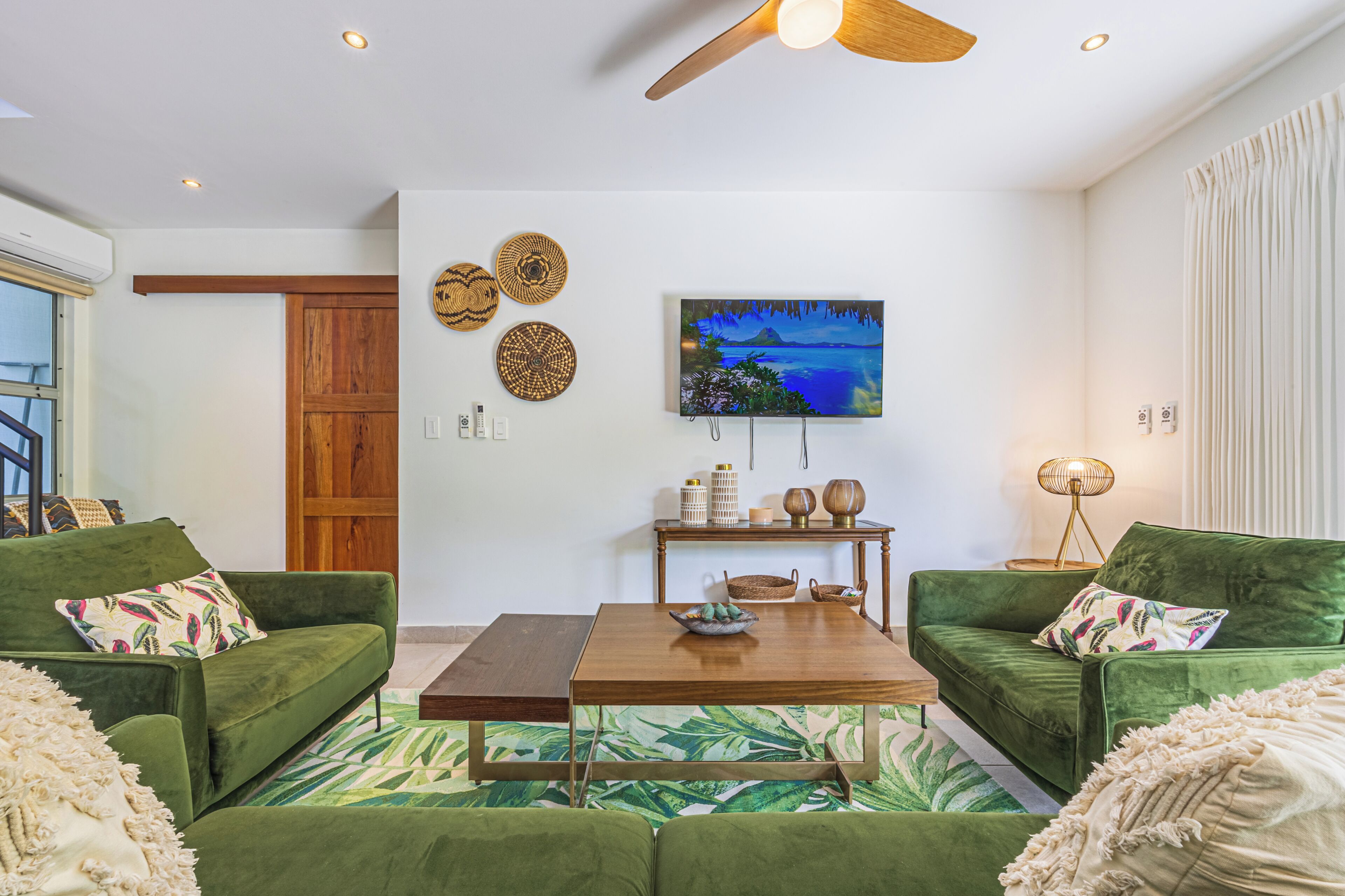 A living room with a green sofa set, a wooden coffee table, a painting on the wall, and a ceiling fan.