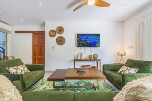Uma sala de estar com sofá verde, mesa de centro de madeira, pintura na parede e ventilador de teto.