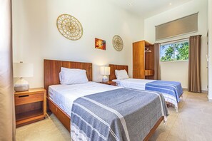 Ein Hotelzimmer mit zwei Betten, Holz-Kopfteilen, Nachttischen mit Lampen, einem Kleiderschrank und einem Fenster mit Vorhängen.