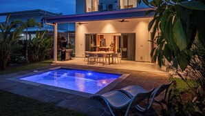 Una casa moderna de dos pisos con piscina, zona de comedor exterior y terraza cubierta.