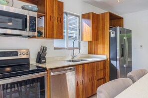 Una cocina compacta con armarios de madera, un refrigerador de acero inoxidable, un microondas y un lavavajillas.