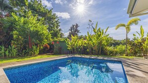Una piscina con agua cristalina azul, rodeada de abundante vegetación y un cielo despejado.