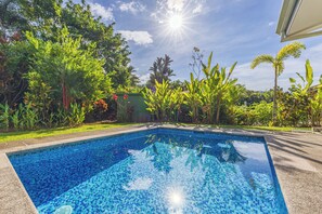 Una piscina amb aigua cristal·lina i blava, envoltada de vegetació exuberant i un cel serè.