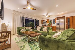 Una sala de estar moderna con sofás verdes, una mesa de centro de madera y un comedor con una cocina al fondo.