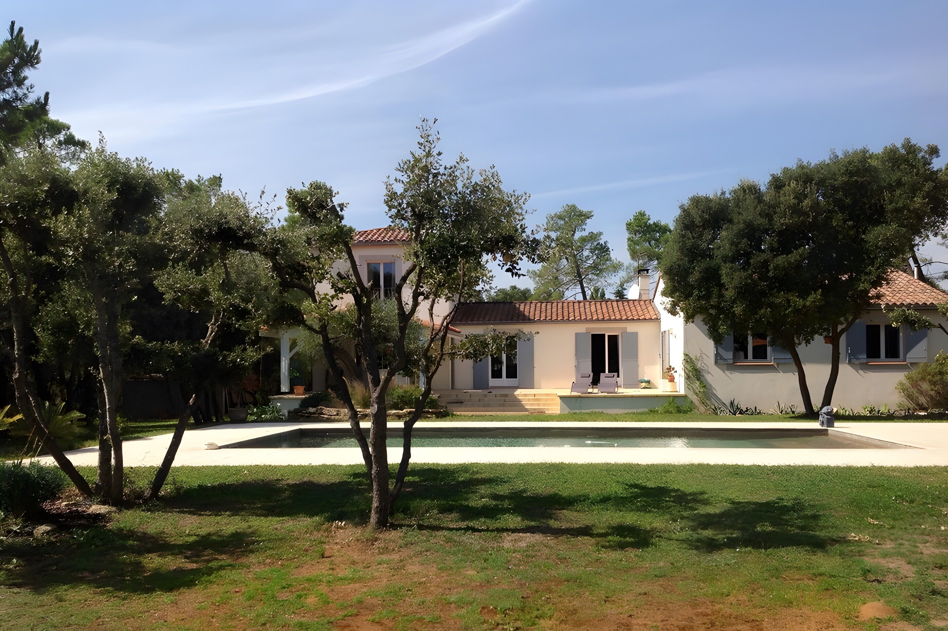 Une maison à deux étages avec une piscine, entourée d’arbres et d’une pelouse bien entretenue.
