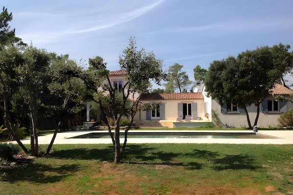 Une maison à deux étages avec une piscine, entourée d’arbres et d’une pelouse bien entretenue.