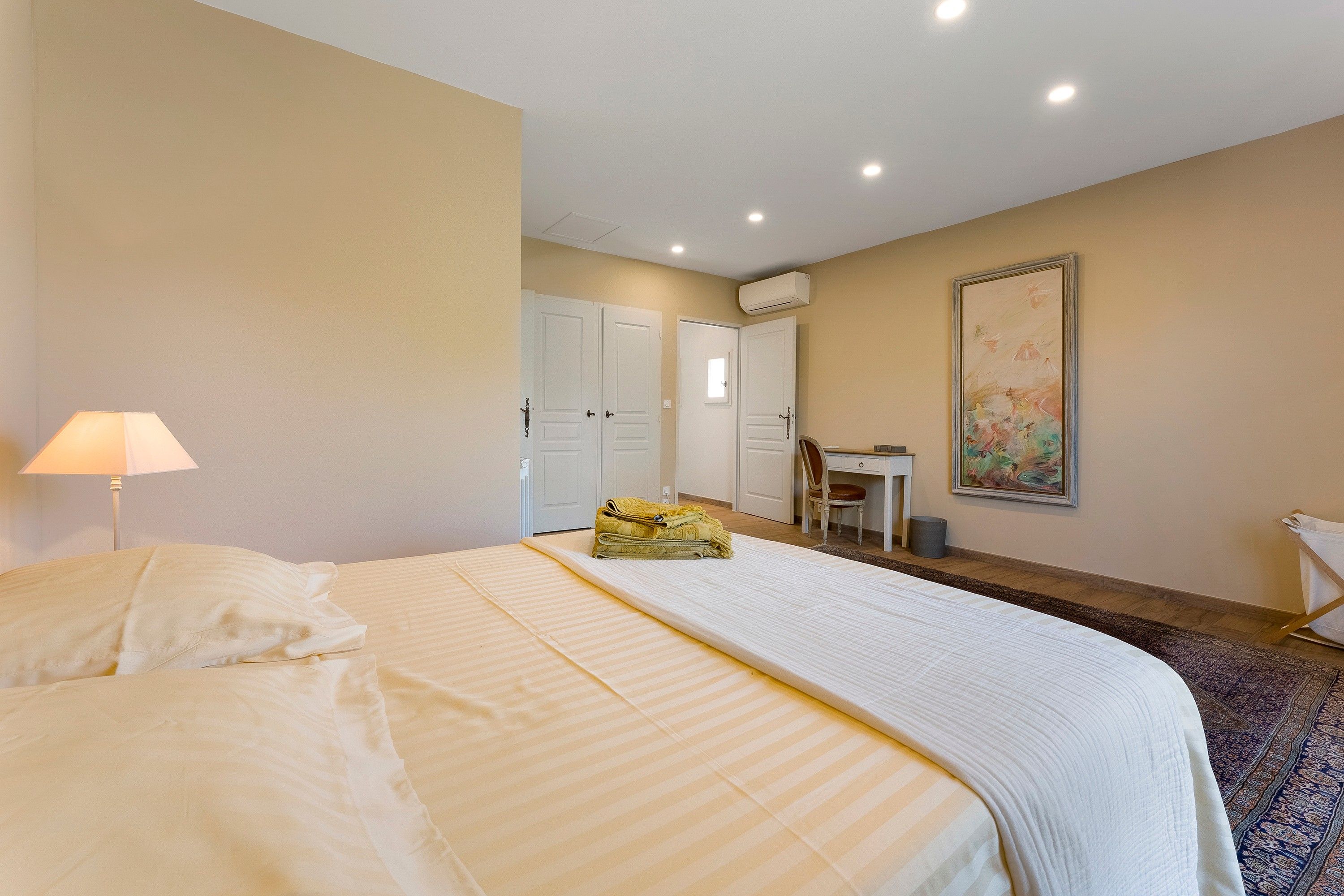 Une chambre d’hôtel avec un lit, un bureau, une chaise, un appareil de climatisation et un tableau au mur.