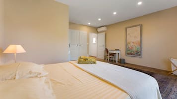 A hotel room with a bed, a desk, a chair, an air conditioning unit, and a painting on the wall.
