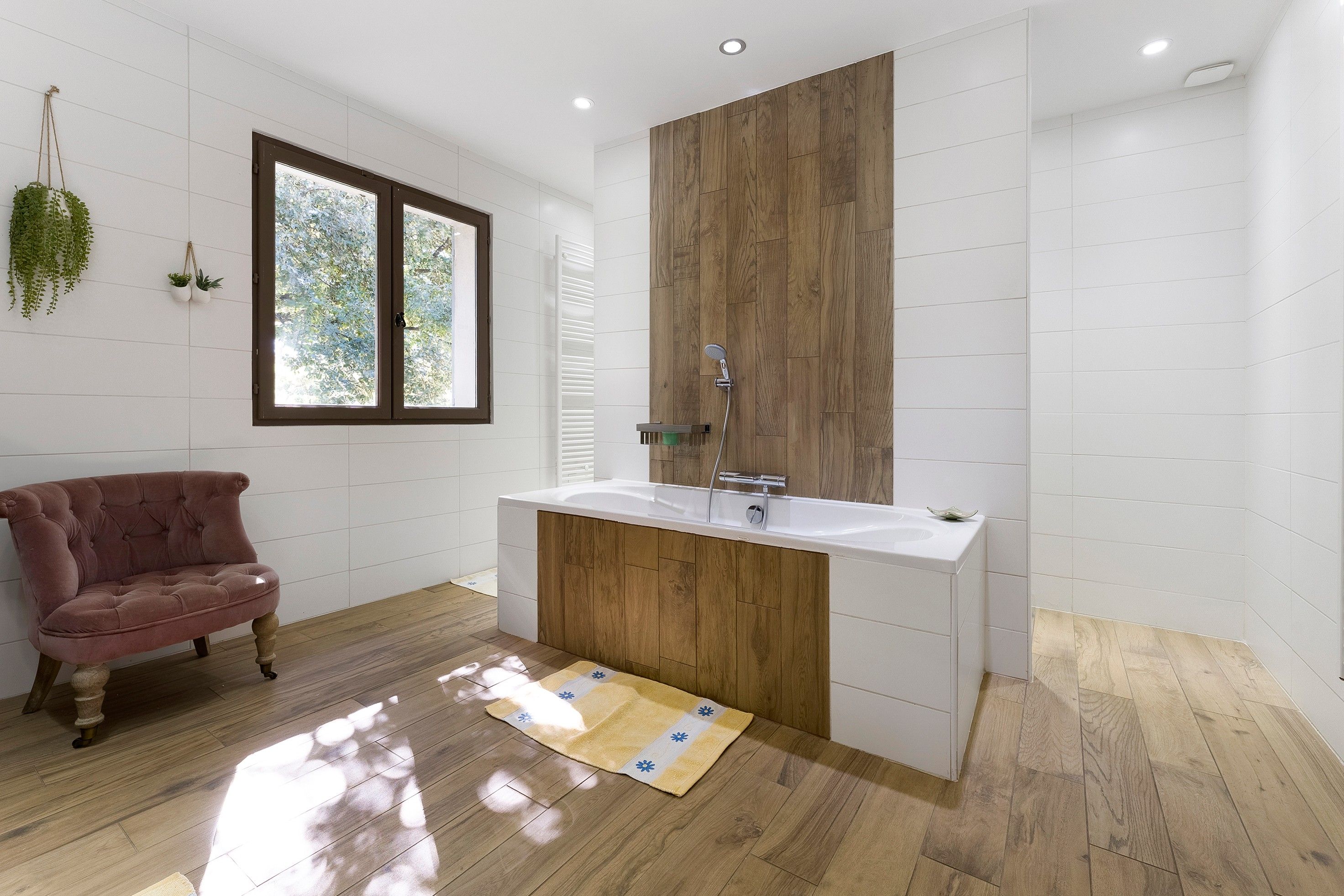 Un baño moderno con un tocador de madera, un ventanal grande y una silla rosa.