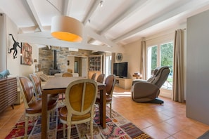 A spacious dining area with a large table and chairs, a stone fireplace, and a television in the background.