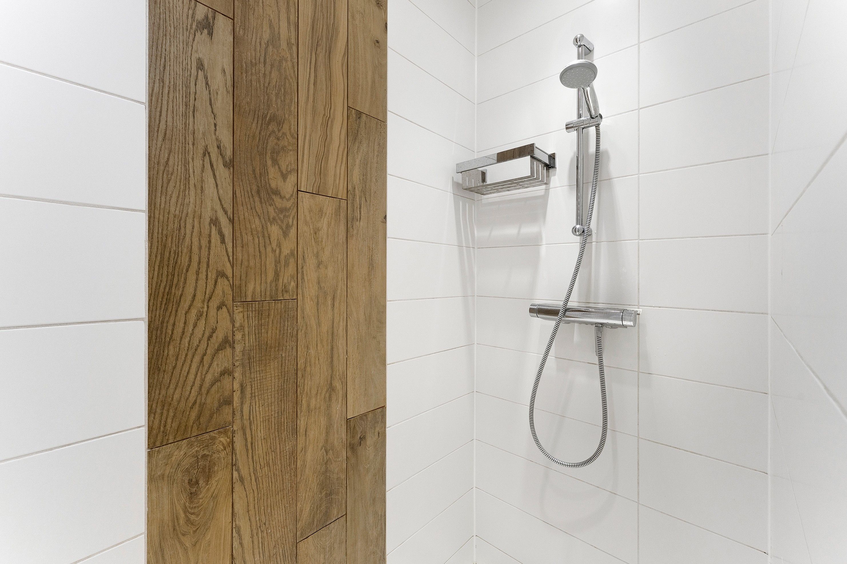 Eine Dusche mit Handbrause und Bedienfeld an der Wand.