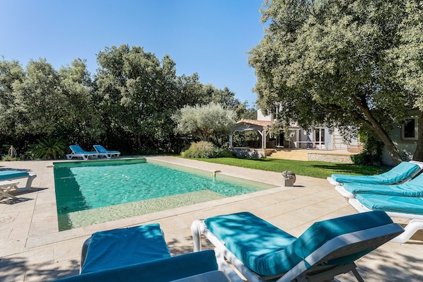 A swimming pool with lounge chairs, surrounded by trees and a house.