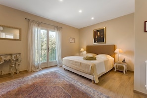 A bedroom with a large bed, a nightstand, a lamp, a mirror, and a window with curtains.