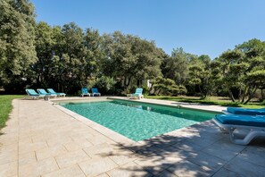 A swimming pool with lounge chairs, surrounded by trees.