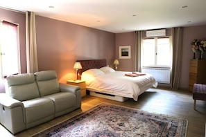 Une chambre à coucher comprenant un lit, une chaise, une table de chevet, une lampe, une fenêtre avec des rideaux et un radiateur.