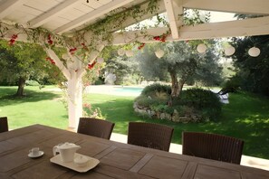 Une terrasse couverte avec une table préparée pour le thé, entourée d’une végétation luxuriante et offrant une vue sur une piscine.