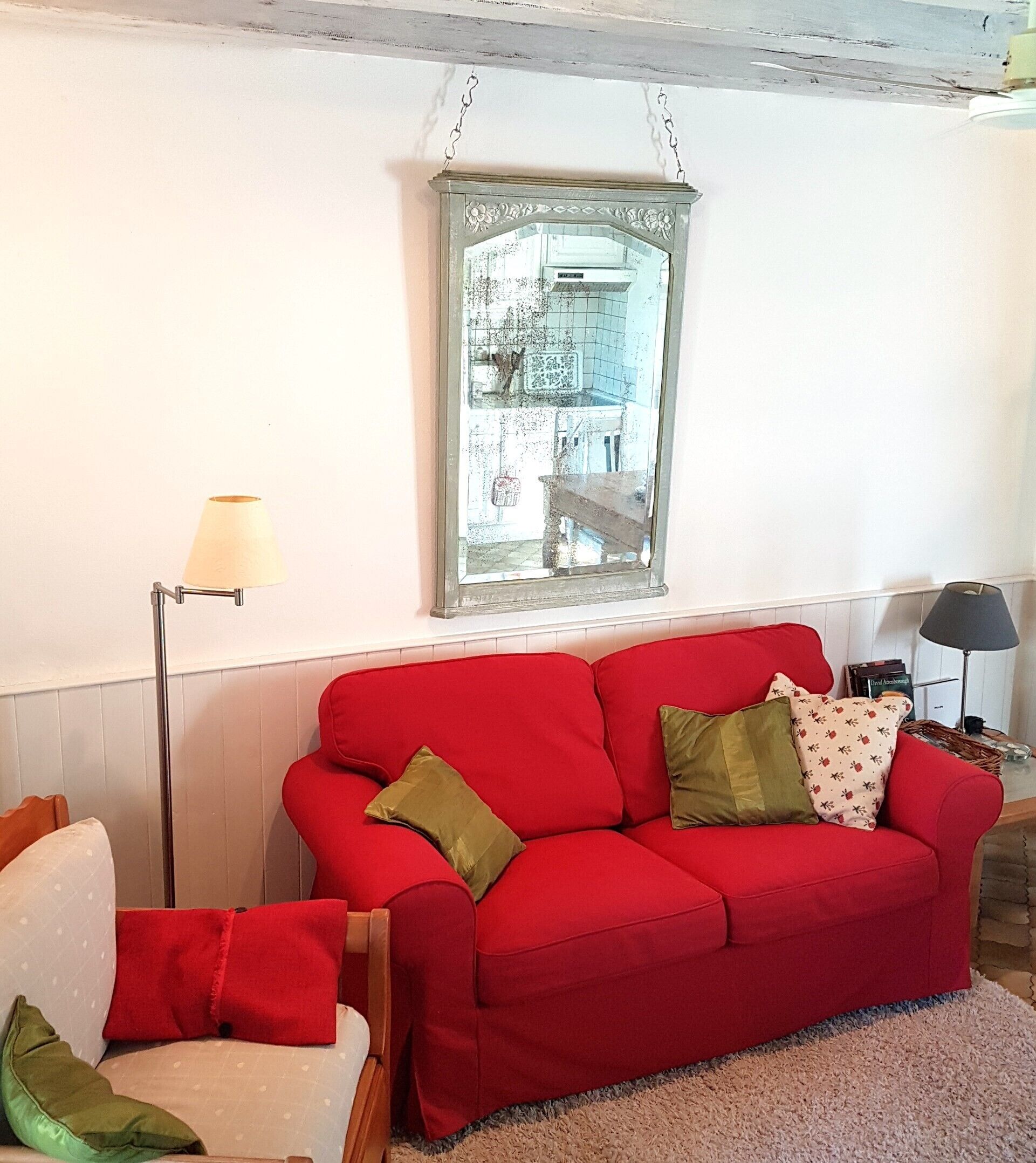 Ein rotes Sofa mit Kissen, eine Stehlampe, ein Spiegel und ein Sessel mit Sitzkissen.