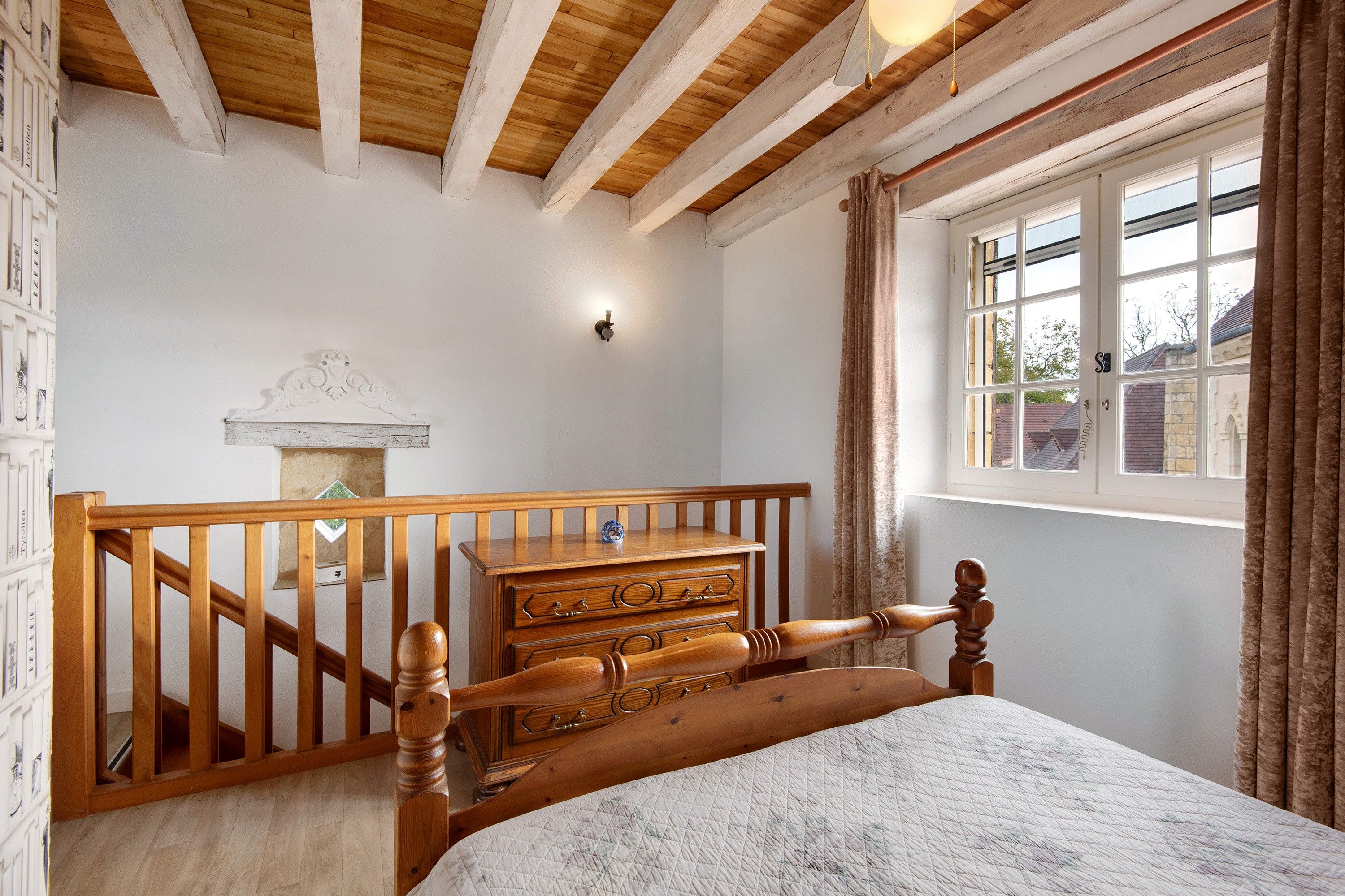 A bedroom with a wooden bed, a dresser, a staircase, and a window with curtains.