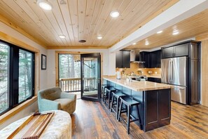 Une cuisine moderne dotée d’un îlot central, de meubles noirs, d’appareils électroménagers en acier inoxydable et d’un plafond en bois.