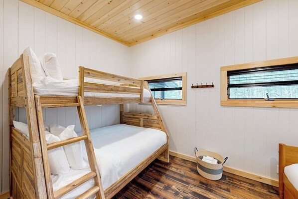 Une chambre avec un lit superposé, une échelle, une fenêtre et un plancher en bois.