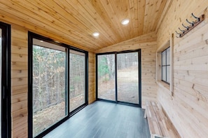 Interior de una cabaña con paredes de madera, grandes puertas correderas de vidrio y un banco.