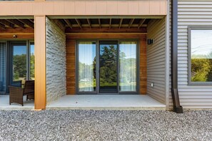 A modern building with a covered patio area, large sliding glass doors, and a gravel ground surface. - 3 BR townhouse with balcony - fireplace - near beach (Lake George)