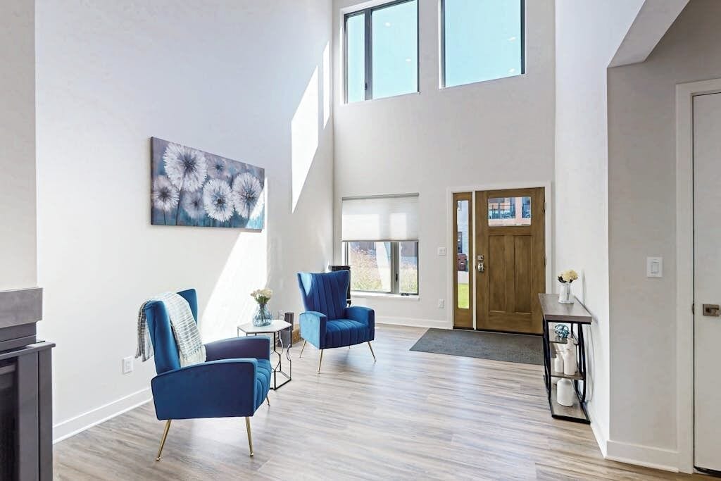 A spacious living area with a high ceiling, two blue armchairs, a coffee table, and a painting on the wall.